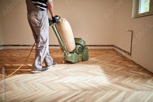 Repairman restoring parquet with a sanding machine.
