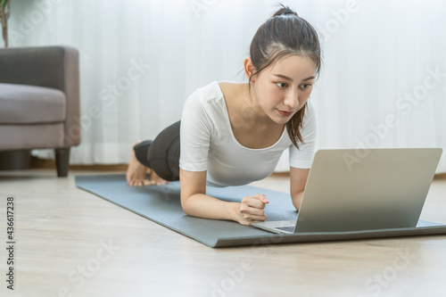 Fit, sporty asian young beautiful woman, girl doing yoga pose planking, watching trainer online on laptop computer, training in living room. Workout fitness exercise people in sportswear at home.