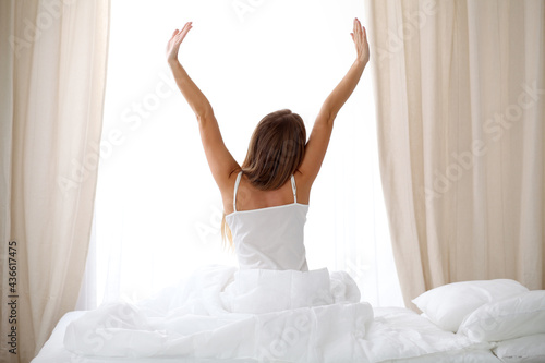 Woman stretching in bed after wake up, back view, entering a day happy and relaxed after good night sleep. Sweet dreams, good morning, new day, weekend, holidays concept