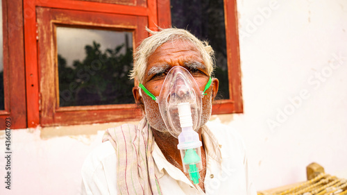 Old Indian man infected with Covid 19 disease. Patient inhaling oxygen wearing mask with liquid Oxygen flow. photo