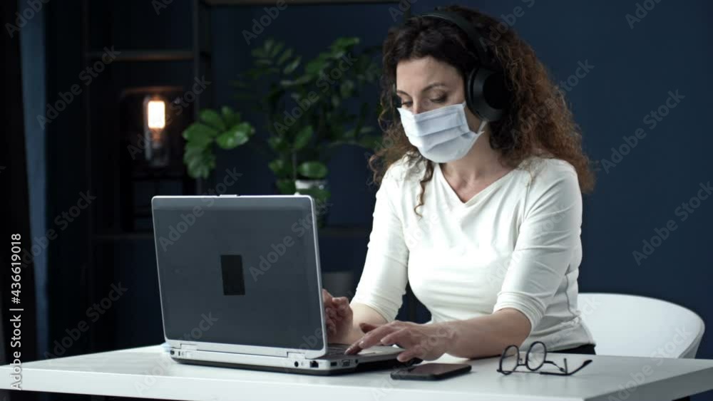 Office work during the coronavirus epidemic. Business woman in a medical mask is looking into a laptop webcam and talking to someone. Office work during the coronavirus epidemic. Business woman in a medical mask is looking into a laptop webcam and talking to someone.