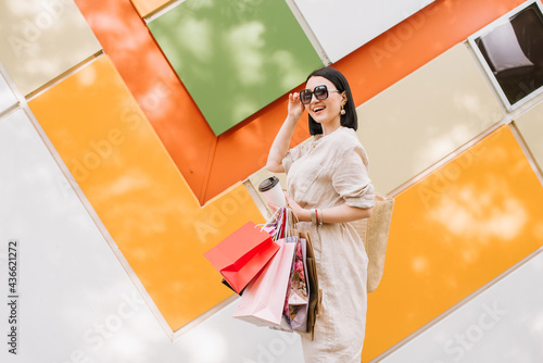 Brunette woman with shopping bags posing at the colored wall of the store
