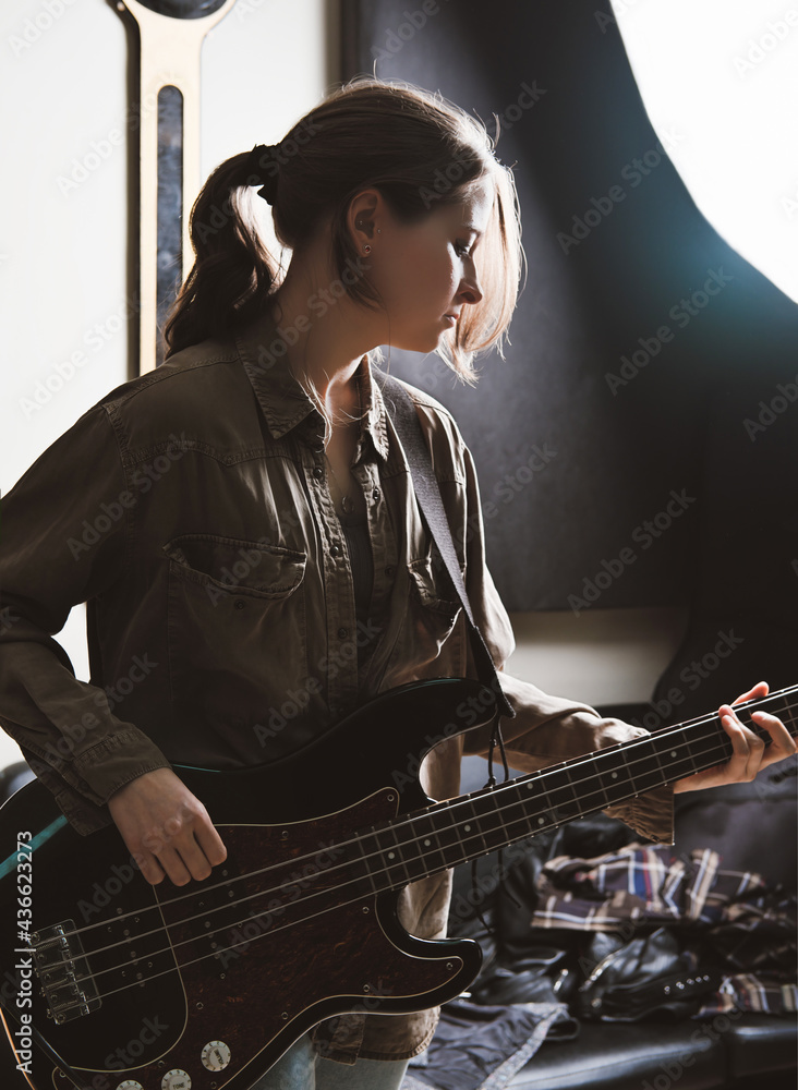 young woman playing electric bass guitar in a studio. rock musician rehearsal room. sound recording and check - obrazy, fototapety, plakaty 