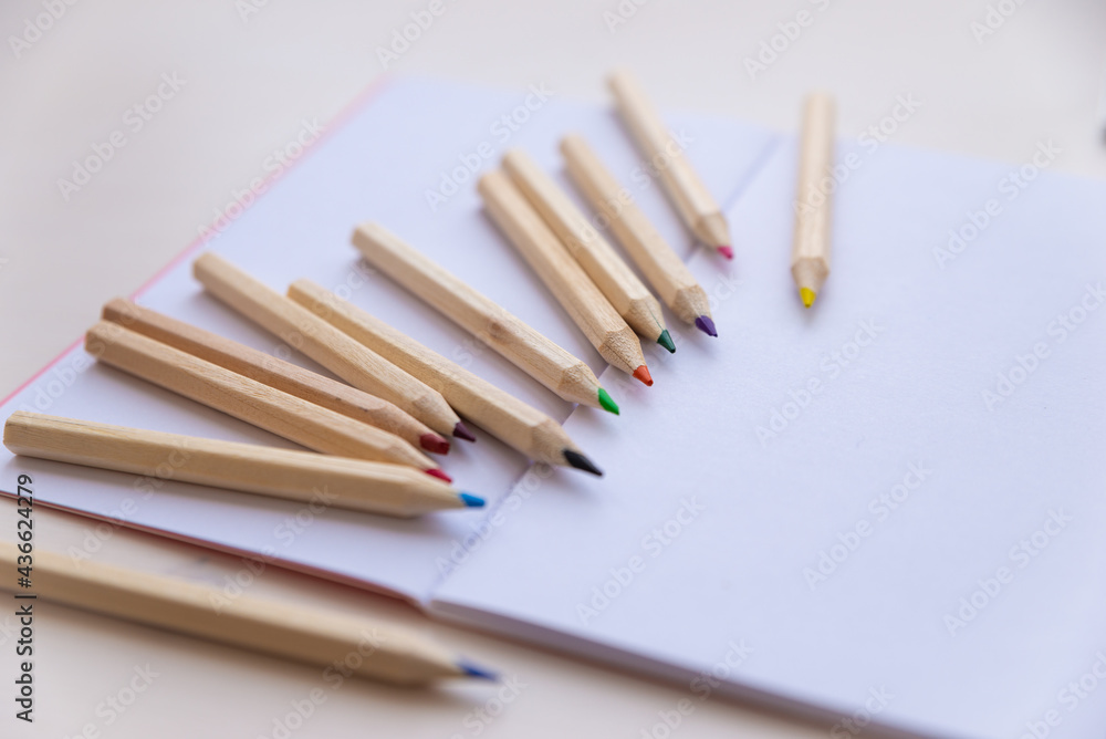 Open white notebook, with colored crayons beside it, penknife and drawing of a colored flower. Open white notebook, with colored crayons beside it, penknife and drawing of a colored flower.