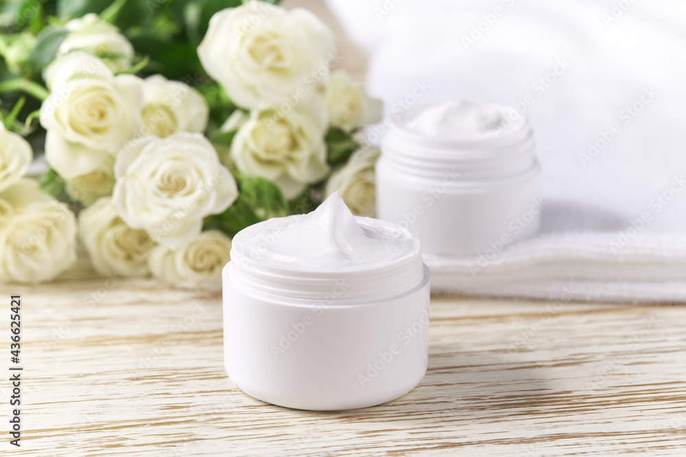 Moisturizing cosmetic sensitive skin, hygiene skin care product or relaxing makeup mask in a white jar with a towel on a background of white roses. Moisturizing cosmetic sensitive skin, hygiene skin care product or relaxing makeup mask in a white jar with a towel on a background of white roses.