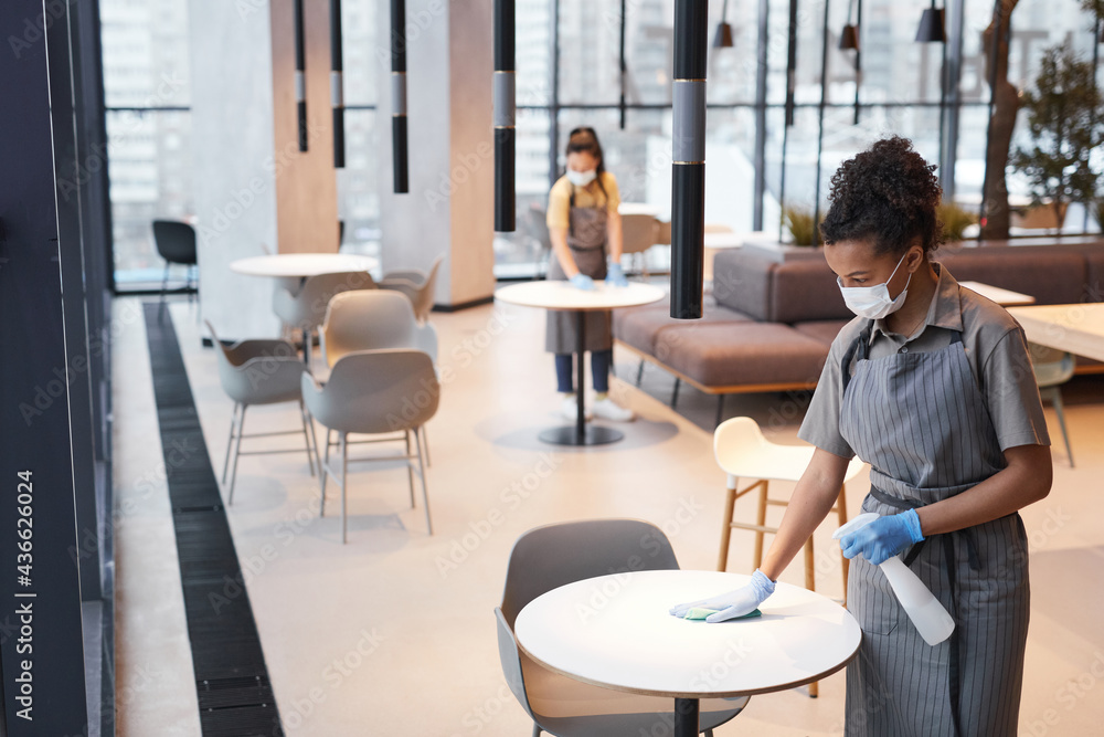 Portrait of two female workers wearing masks while cleaning tables in cafe interior, covid safety concept, copy space Portrait of two female workers wearing masks while cleaning tables in cafe interior, covid safety concept, copy space