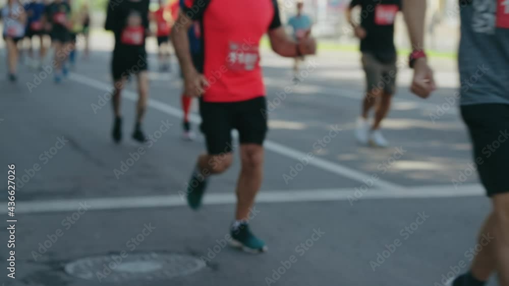 Partial view athletes running marathon on asphalt road in slow motion. Blurred sports background. Tracking shot contestants of street race. Concept of healthy lifestyle Partial view athletes running marathon on asphalt road in slow motion. Blurred sports background. Tracking shot contestants of street race. Concept of healthy lifestyle