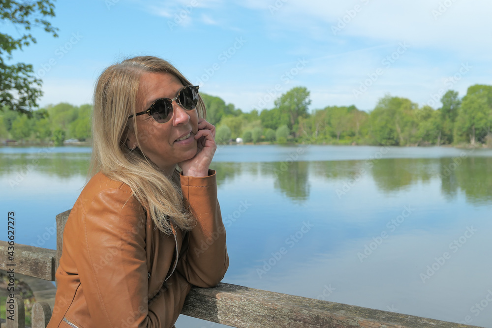 Fototapeta premium Portrait of a woman with long blond hair in nature. Lake and vegetation blurred voluntarily in the background.