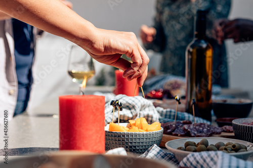 female hand holding toothpick piercing a piece of melon on party table with aperitif snacks. Incidental people in the foreground. photo