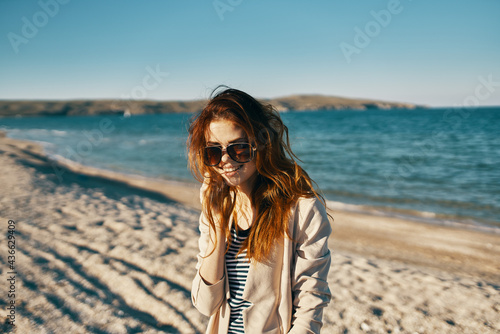 red-haired woman on the beach wearing glasses near the sea beige coat t-shirt model