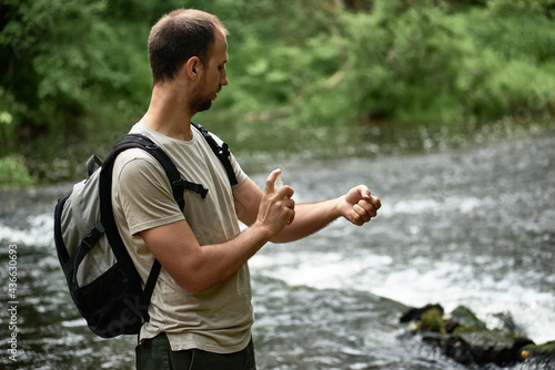 Fotografi Side view of a hiker in a shirt with a backpack near the river spraying insect repellent on skin