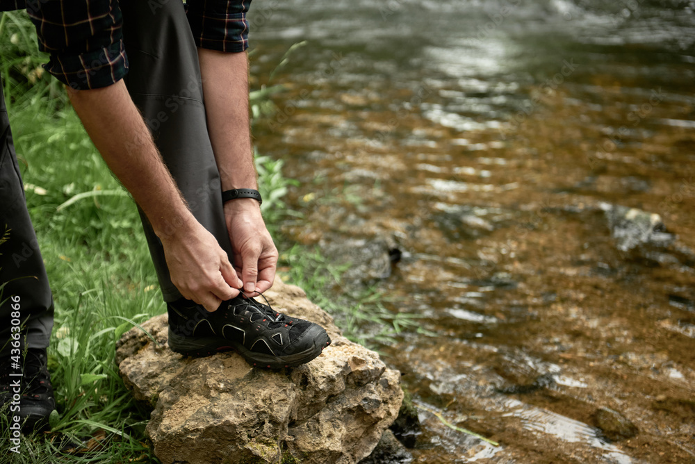 Tourist tying shoelaces placing his foot on a large stone by the stream Tourist tying shoelaces placing his foot on a large stone by the stream