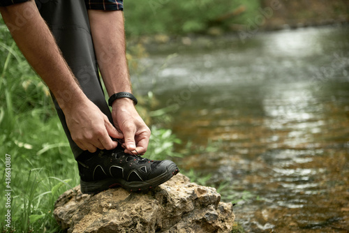 Male hiker tying shoelaces placing his foot on a large stone by the stream