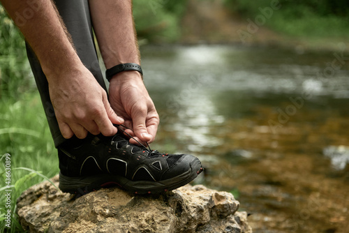Male hiker tying shoelaces placing his foot on a large stone by the creek