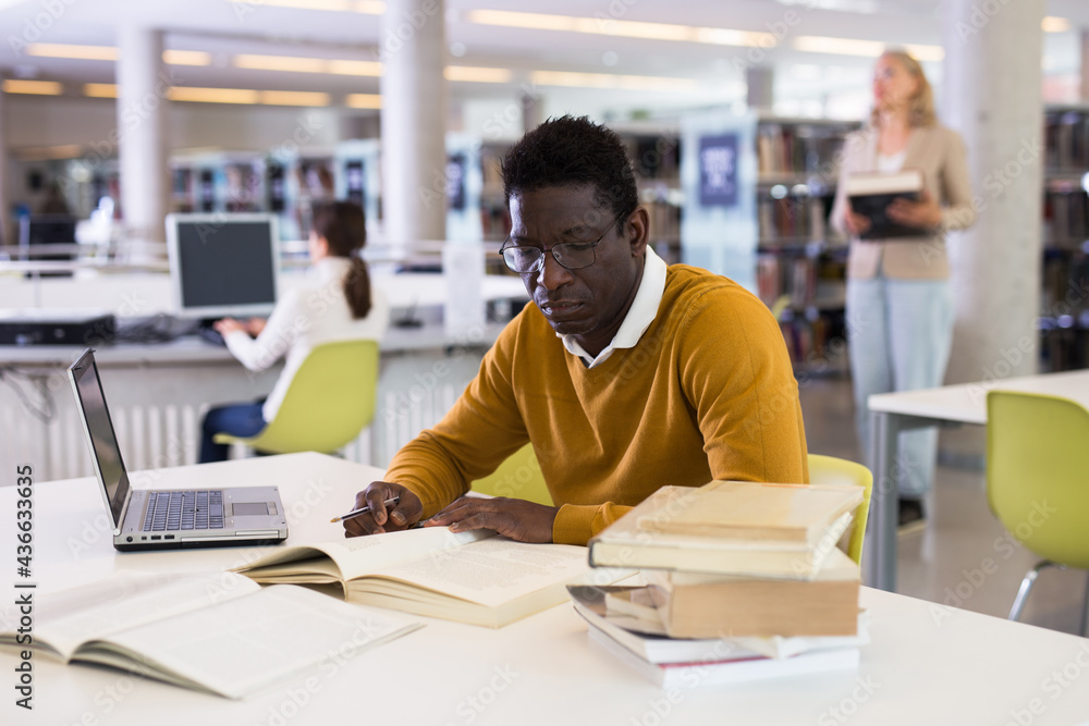 Fototapeta premium Confident african-american man working on laptop in public library. High quality photo