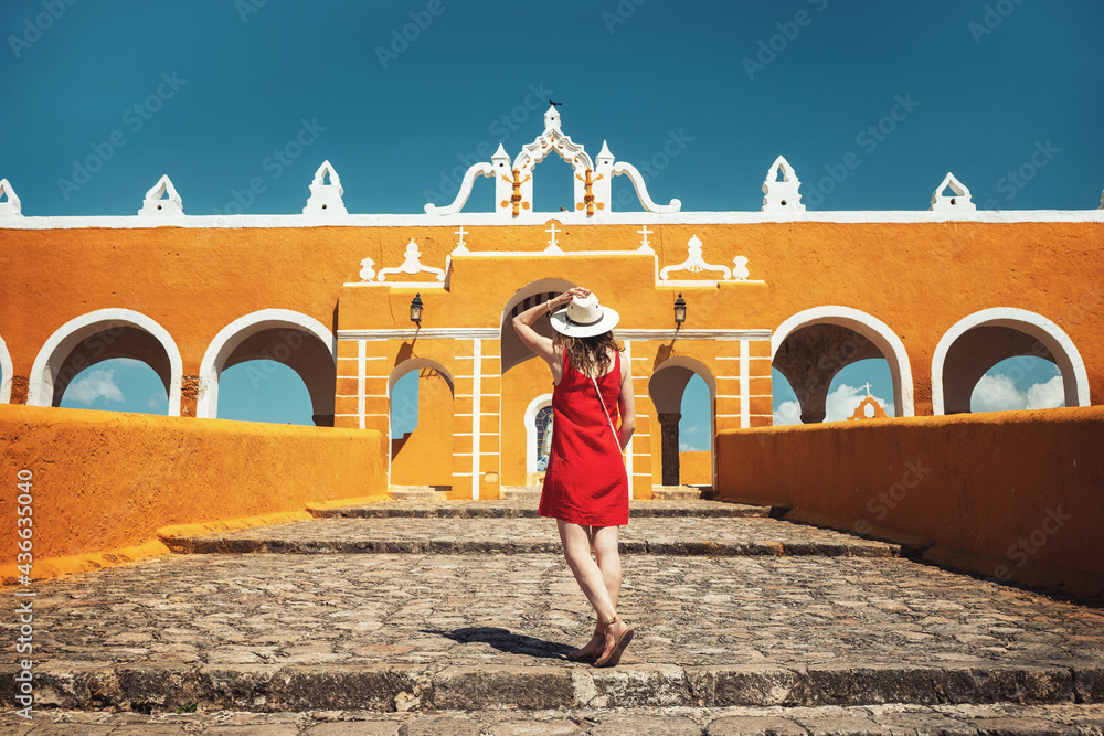 A young woman in a red dress and hat travels through the yellow city of Izamal, Mexico. Lifestyle. Travel to Mexico. Beautiful multicolored cities in Mexico