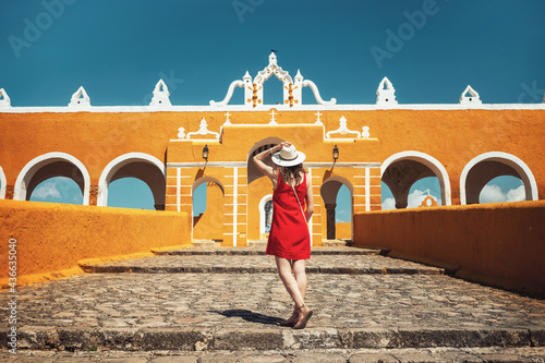 A young woman in a red dress and hat travels through the yellow city of Izamal, Mexico. Lifestyle. Travel to Mexico. Beautiful multicolored cities in Mexico photo