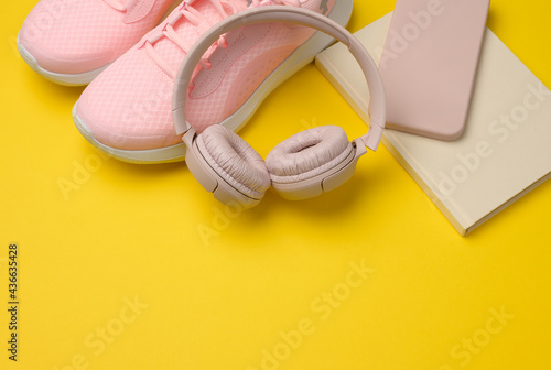 pair of pink sneakers, wireless headphones, a smartphone and a smart watch on a yellow background