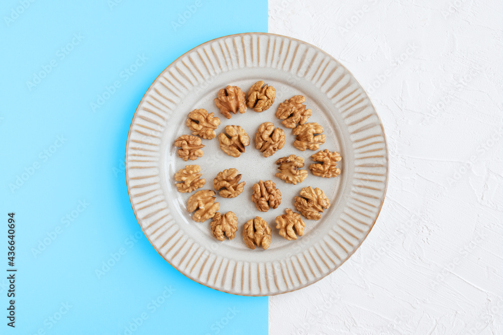 Walnuts in a plate on sky blue and white background, flat lay.