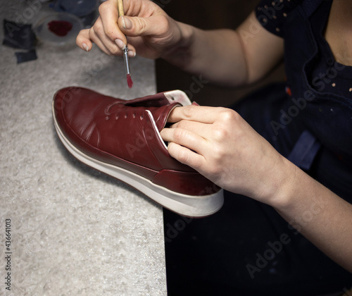 a woman shoemaker, in a workshop, under the light of a lamp, paints shoes with a brush. Shoe repair, dyeing, family business, traditions.