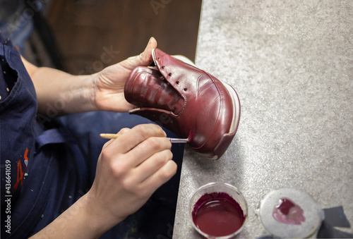 a woman shoemaker, in a workshop, under the light of a lamp, paints shoes with a brush. Shoe repair, dyeing, family business, traditions.