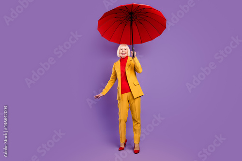 Full size photo of cheerful short hairdo aged lady hold umbrella wear yellow costume isolated on purple background