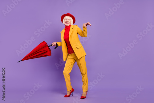 Full body profile photo of funny short hairdo elder lady wear yellow suit cap umbrella isolated on purple background © deagreez