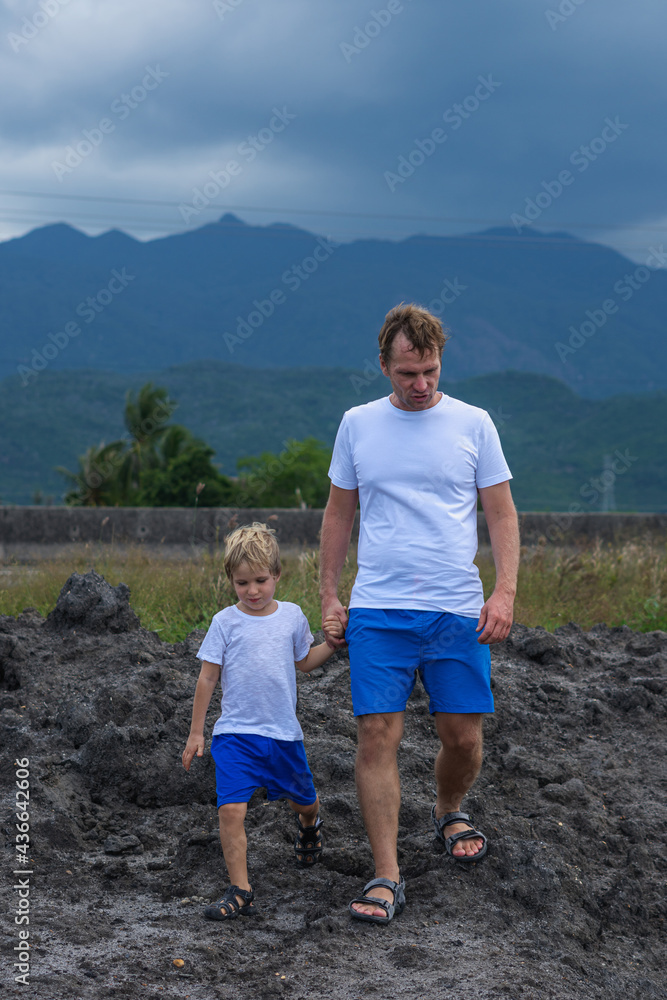 VERTICAL Serious Father son or adult younger brother walk together look for adventure. Cloudy sky before rain, mountain background. Man talk, hold boy by hand, attentive look Natural science education