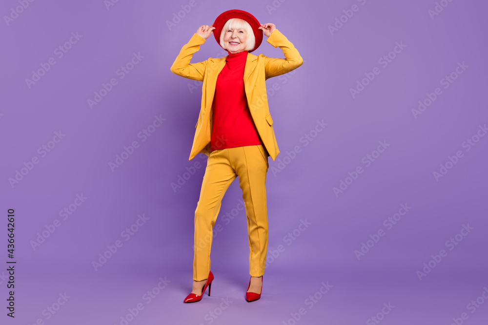 Full length photo of cheerful nice short hairdo aged lady wear yellow suit cap isolated on purple color background Full length photo of cheerful nice short hairdo aged lady wear yellow suit cap isolated on purple color background