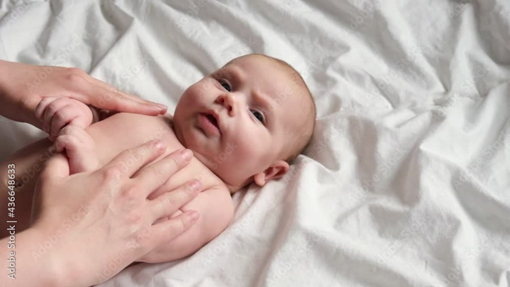 Mother massaging little baby. Newborn Baby skin care concept. Prevention of colic. Female hands doing massage to newborn. Slow motion. Nice caucasian infant baby lying at the back. Portrait. Close up. Mother massaging little baby. Newborn Baby skin care concept. Prevention of colic. Female hands doing massage to newborn. Slow motion. Nice caucasian infant baby lying at the back. Portrait. Close up.