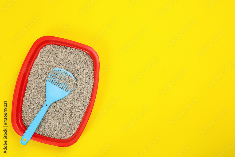 Cat litter tray with filler and scoop on yellow background, top view. Space for text Cat litter tray with filler and scoop on yellow background, top view. Space for text