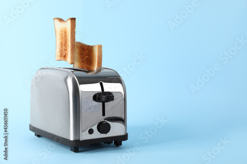 Bread slices popping up from modern toaster on light blue background. Space for text