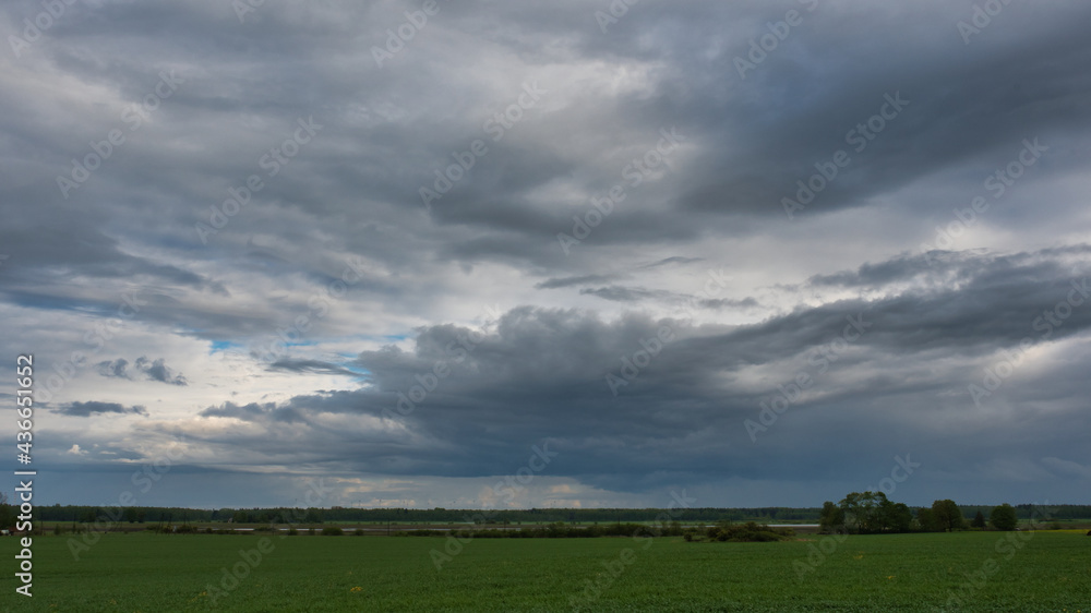 A landscape of a beautiful evening sky with storm clouds over green farmland with islands of trees and bushes, and a forest on the horizon. A landscape of a beautiful evening sky with storm clouds over green farmland with islands of trees and bushes, and a forest on the horizon.