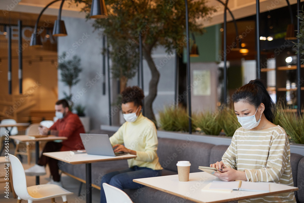 Group of people wearing masks while working at tables in cafe in row