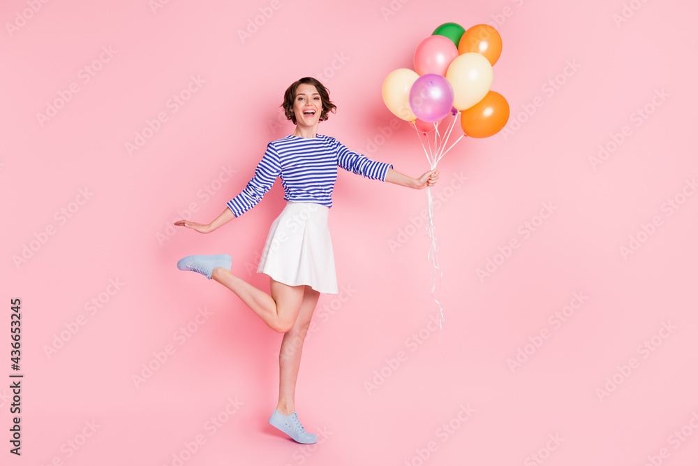 Full size photo of young attractive smiling happy excited cute girl hold balloons raise leg isolated on pink color background Full size photo of young attractive smiling happy excited cute girl hold balloons raise leg isolated on pink color background