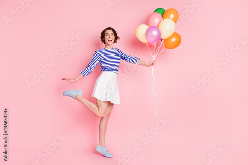 Full size photo of young attractive smiling happy excited cute girl hold balloons raise leg isolated on pink color background
