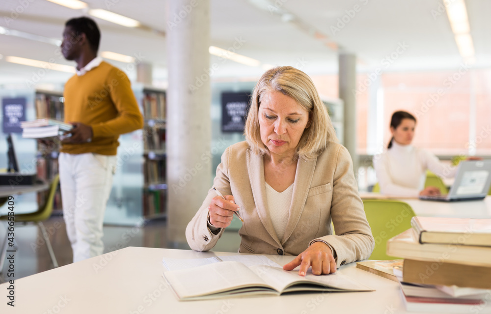 Obraz premium Woman with books sits at table in the library. High quality photo