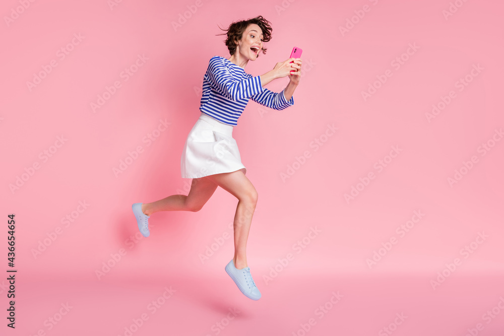 Full size photo of young beautiful smiling excited girl with bob brown hair use phone running isolated on pink color background