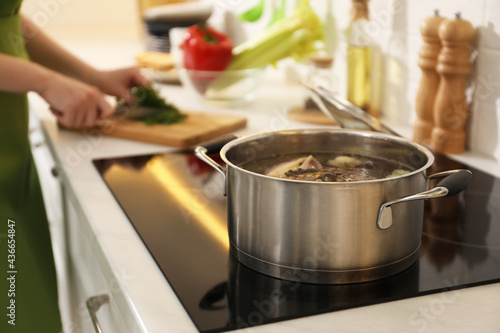 Homemade bouillon recipe. Woman cutting greenery in kitchen, focus on pot