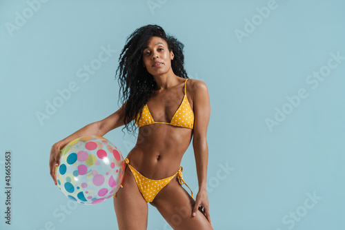 Black brunette woman in swimsuit posing with beach ball