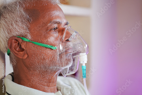 Close up head shot of old man breathing on ventilator oxygen mask at home due to coronavirus covid-19 breathing problem and viral infection photo