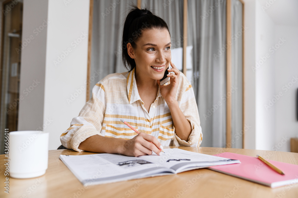 White brunette woman talking on cellphone while doing homework White brunette woman talking on cellphone while doing homework