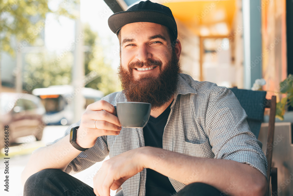Portrait of cheerful bearded hipster man sitting outdoors and holding cup of coffee Portrait of cheerful bearded hipster man sitting outdoors and holding cup of coffee