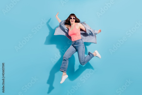 Full length photo of funny young lady jump wear top jeans eyewear isolated on blue color background