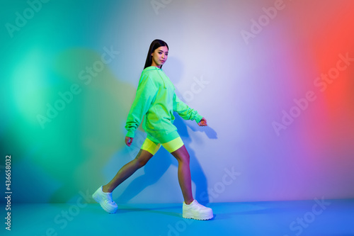 Full length body size profile side view of attractive girl walking wearing sporty clothes isolated over multicolor vivid neon light background