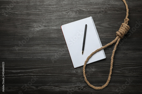 Rope noose and blank notebook with pen on black wooden table, flat lay. Space for text photo