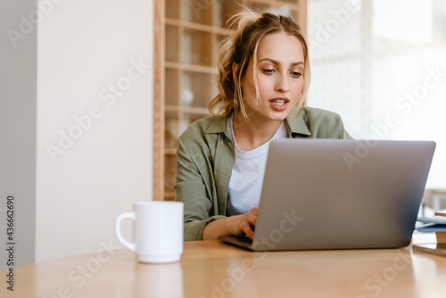 Young white woman using laptop while sitting at table in room