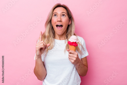 Young australian woman holding an ice cream isolated on pink background pointing upside with opened mouth.