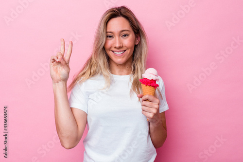 Young australian woman holding an ice cream isolated on pink background showing number two with fingers.