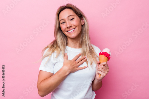 Young australian woman holding an ice cream isolated on pink background laughs out loudly keeping hand on chest.